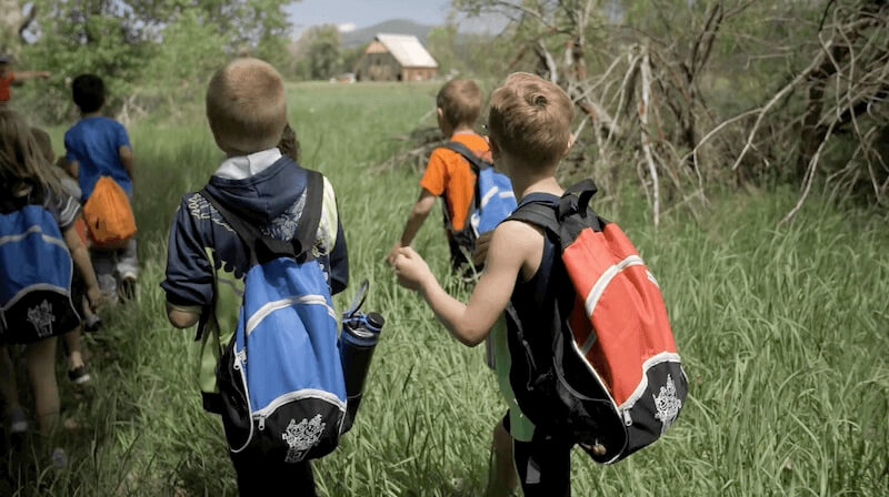 Elementary school kids in backpacks walk toward Olsen Barn