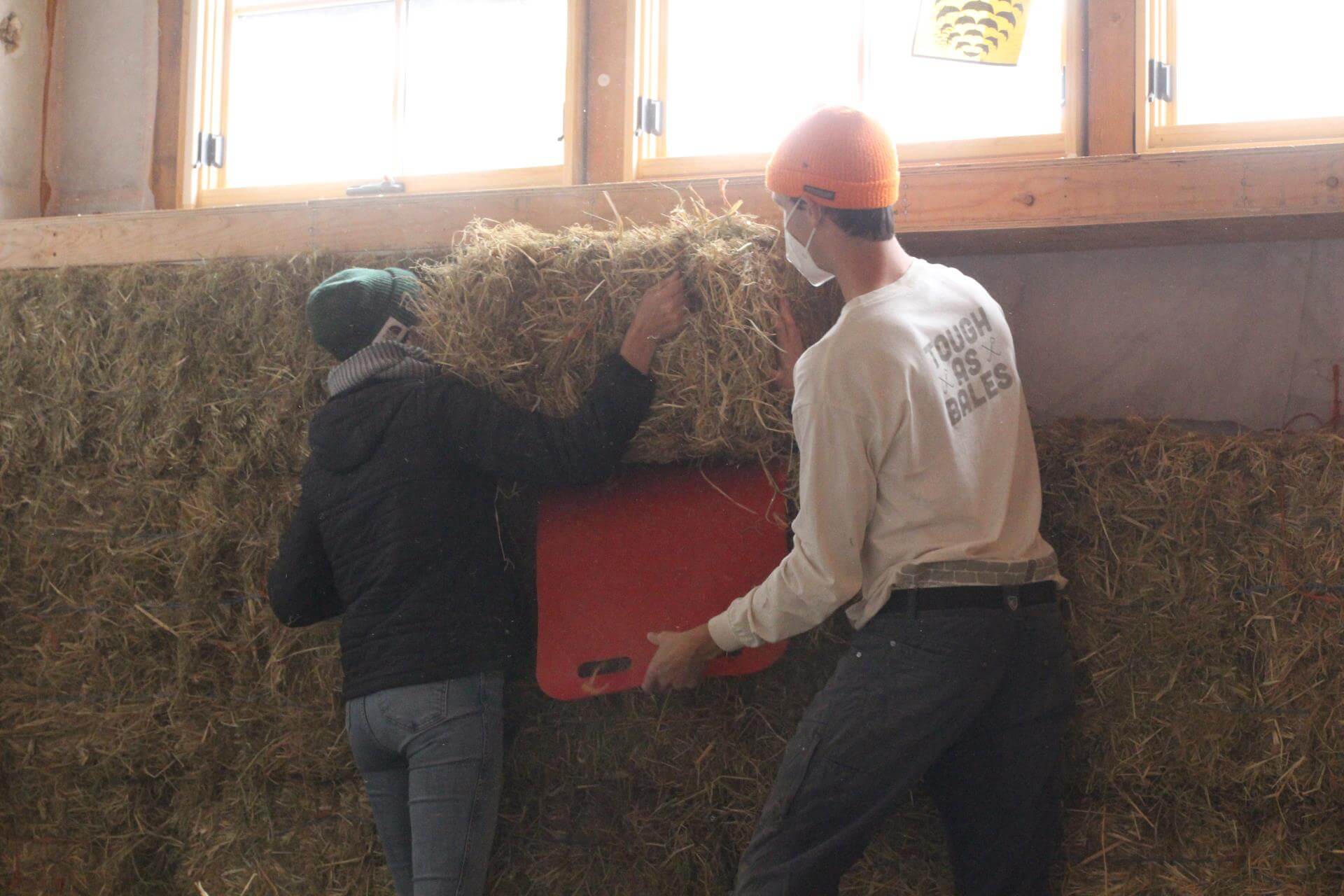 Two volunteers fit a straw bale into a wall.